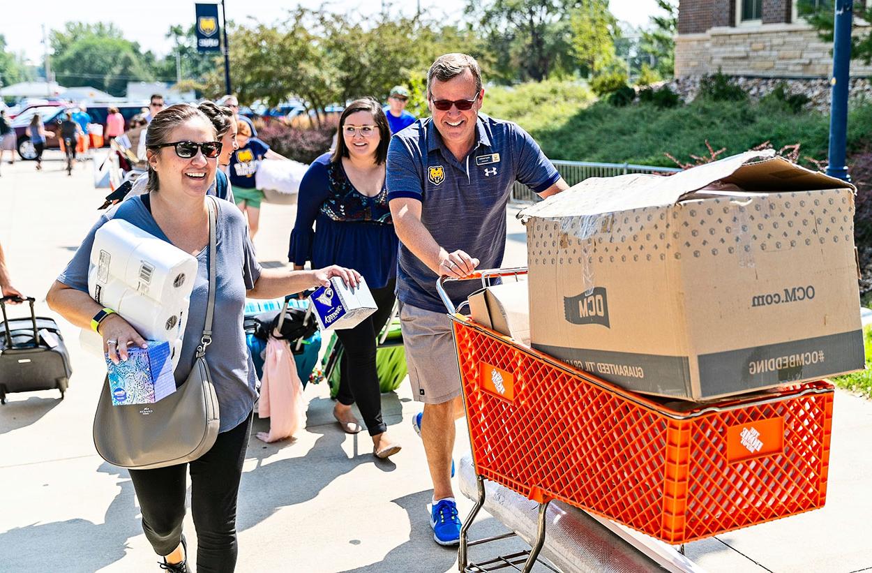 Andy pushes cart of luggage next to students moving into campus.